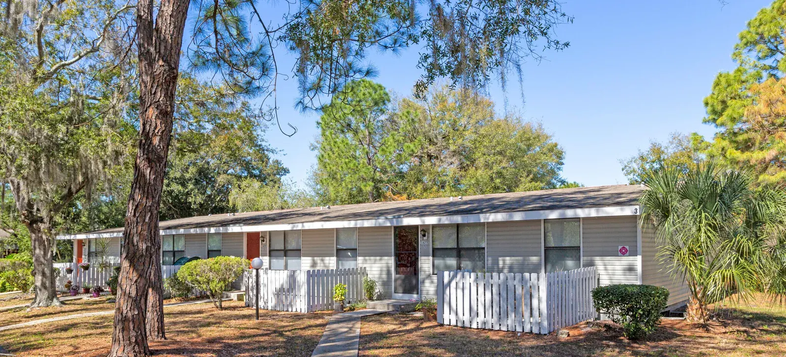 Single-story apartment buildings with fenced patios and mature trees at Lakewood Apartments in Brandon, Florida.