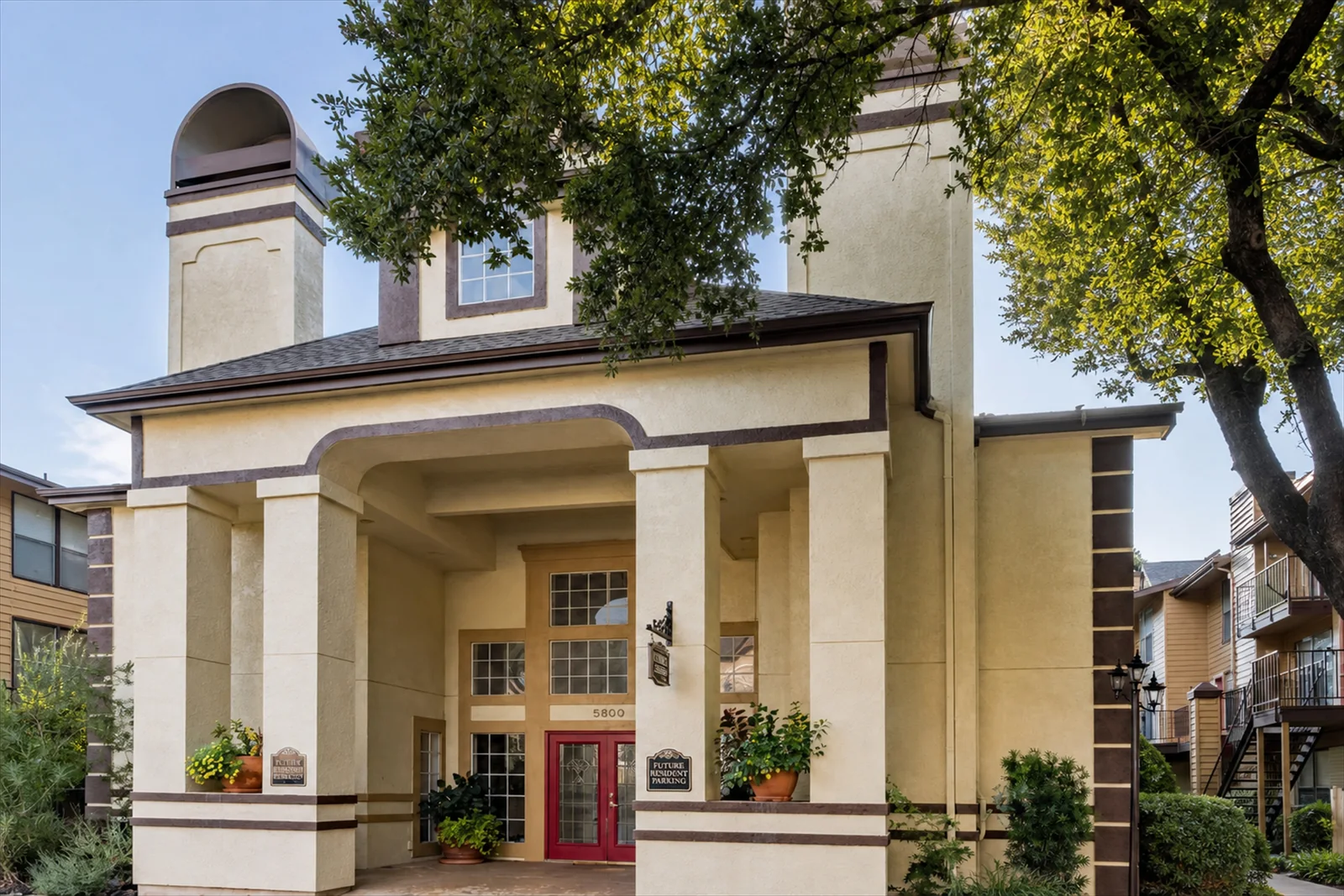 The leasing office exterior at Regal Court Apartments, with its columned entrance, red front door, and mature trees.